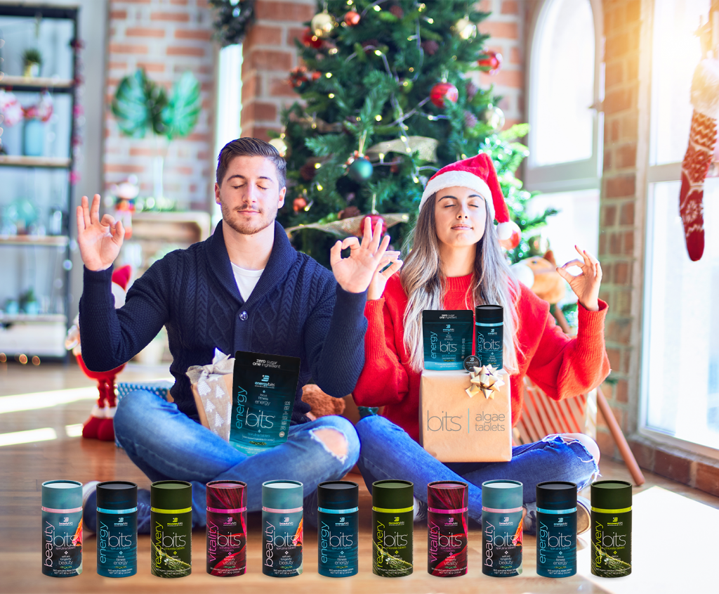 man and woman doing yoga in front of Christmas tree with ENERGYbits products 