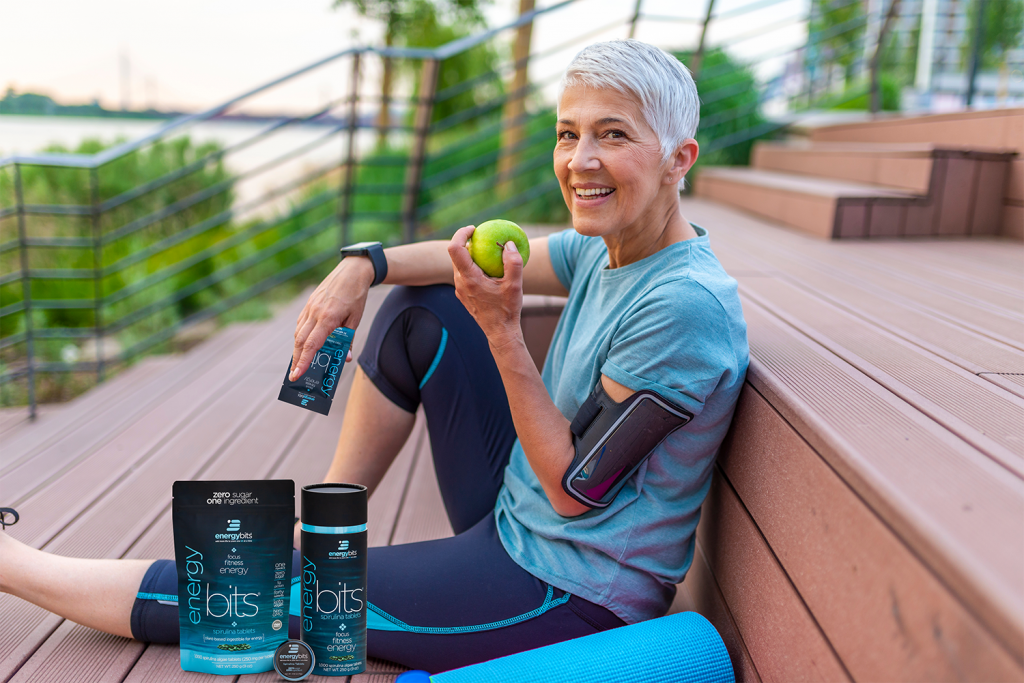 athletic woman sitting with apple and ENERGYbits spirulina 